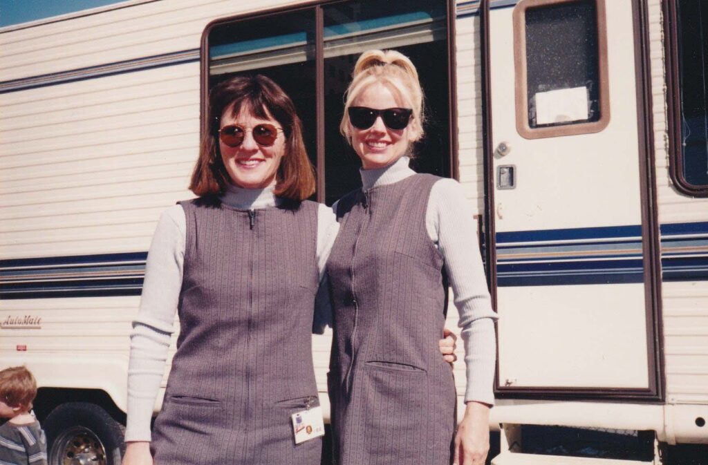 Dressed as baby nannies in matching grey jumpers and white turtlenecks, Elly and her acting friend are on break, standing in front of a trailer on the set of the movie, "Baby Genius."