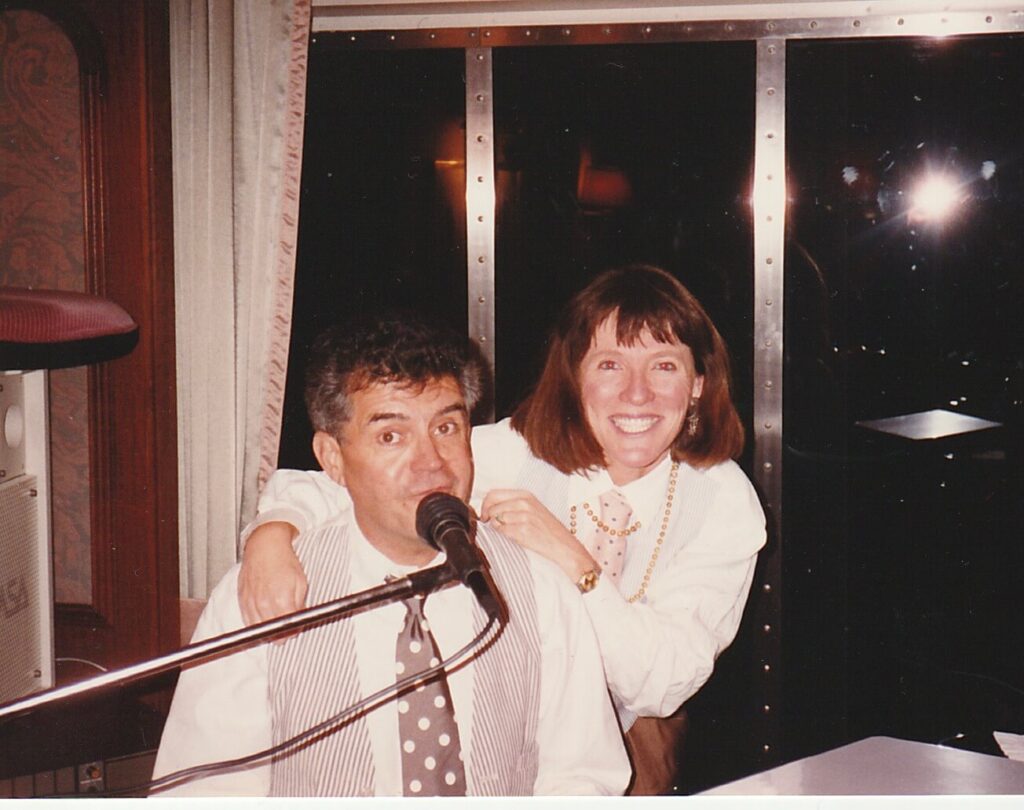 World champion Ragtime piano player, Ron Trotta, is singing into a microphone with his sidekick, Elly McGuire behind him - both crooning on the Crystal Harmony cruise ship.