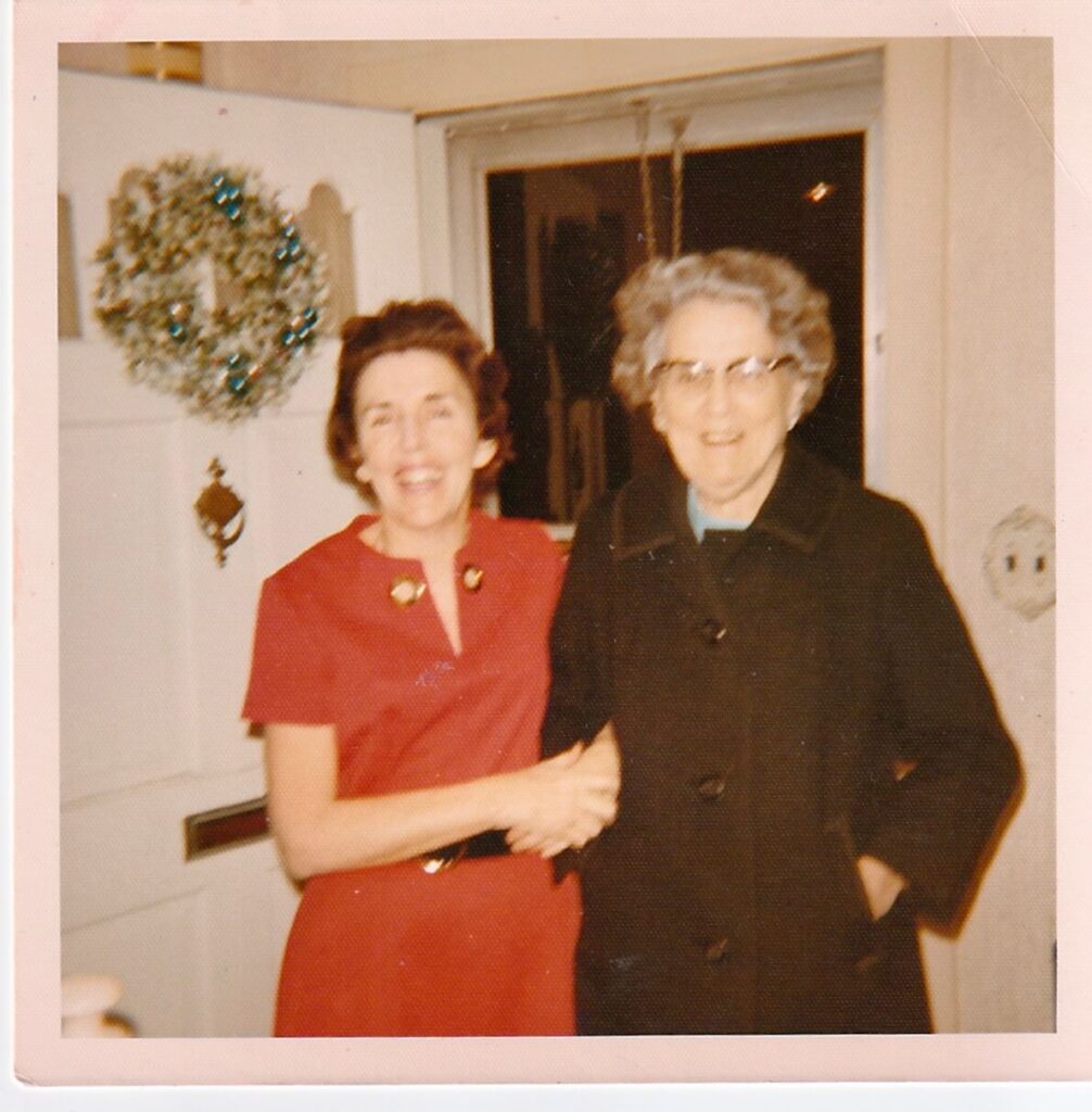 Podcast host, Elly McGuire's mom next to the front door of her home with a wreath hanging on it - posing with her "sweet smelling" Aunt Alice.