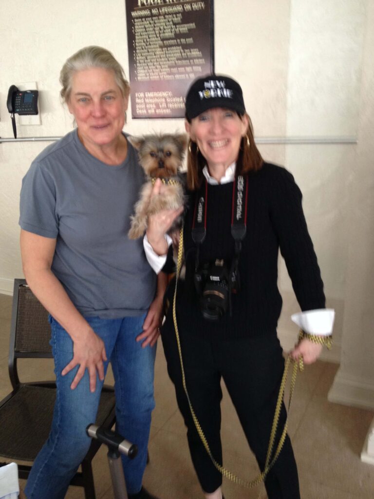 Production Designer Jane Musky in a casual gray t-shirt and jean poses with celebrity pup, Schmitty The Weather Dog, a Yorkshire terrier, and her handler., Author Elly McGuire wearing a black New Yorkie baseball hat, black sweater with white shirt and jeans - on the set of the Empire TV Show set at the Hilton Chicago.